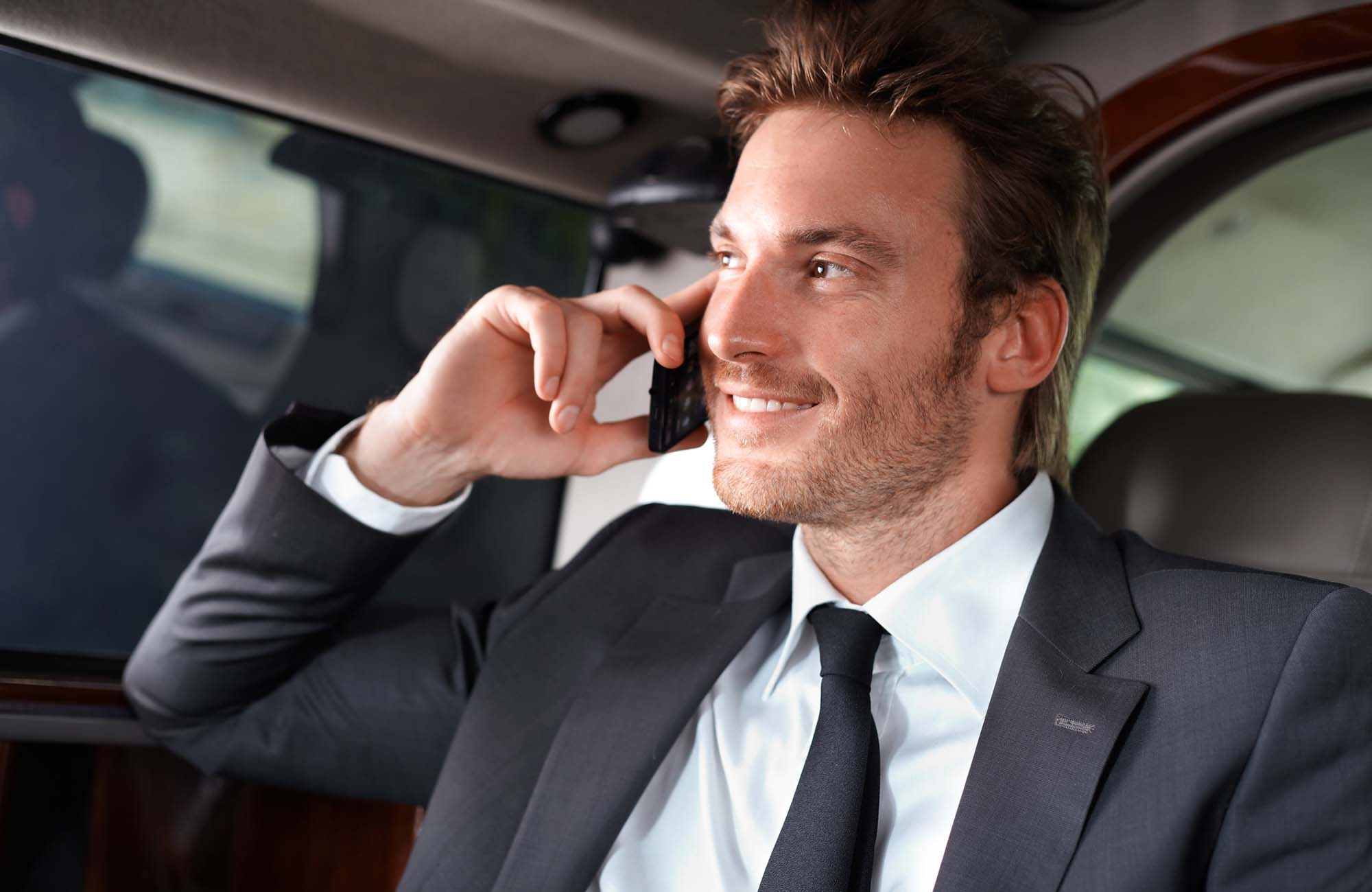 Elegant man in luxury car. Elegant businessman traveling in luxury car, talking on mobile phone, smiling.
