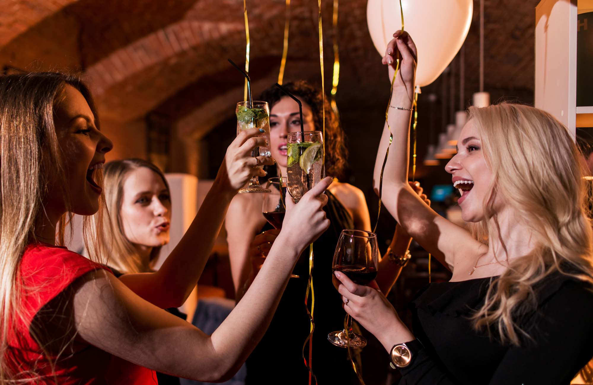 Happy attractive young women having birthday party laughing, dancing, singing, enjoying the night in stylish restaurant.